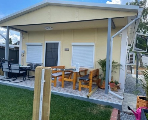 ein Haus und davor sind zwei Tische mit vier Sesseln und zwei Bänken
